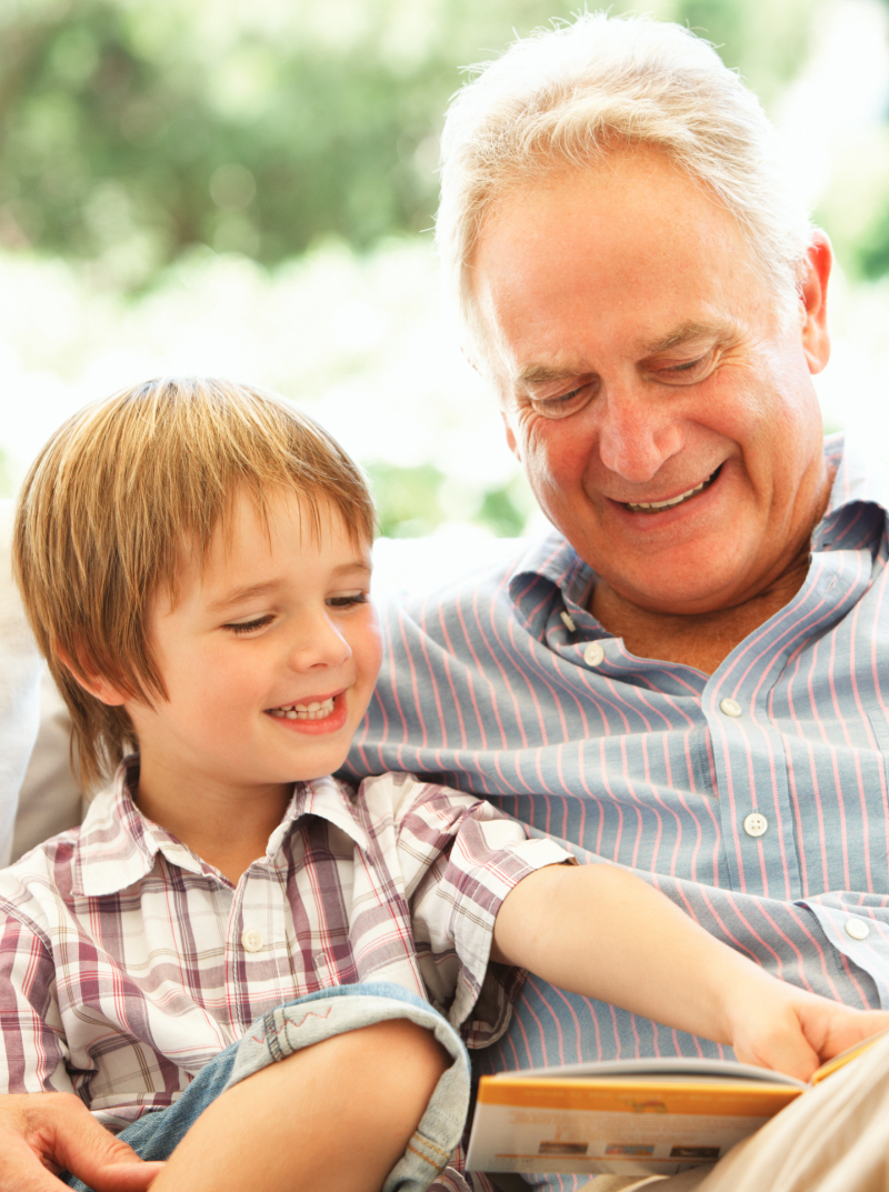 Dědeček s vnukem sedí venku na lavici a čtou pohádky