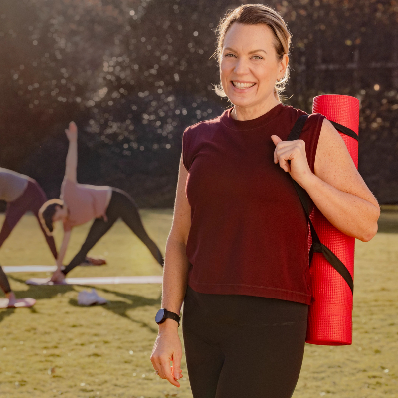 Usmívající se žena s cvičící podložkou přes rameno