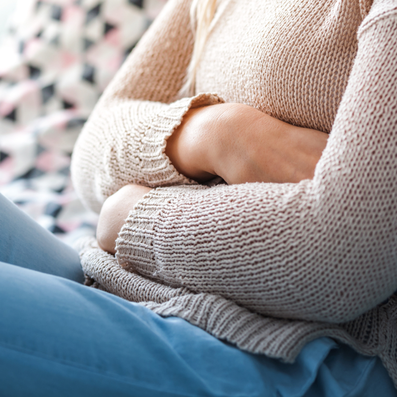 Sedící žena na gauči a držící se za břicho