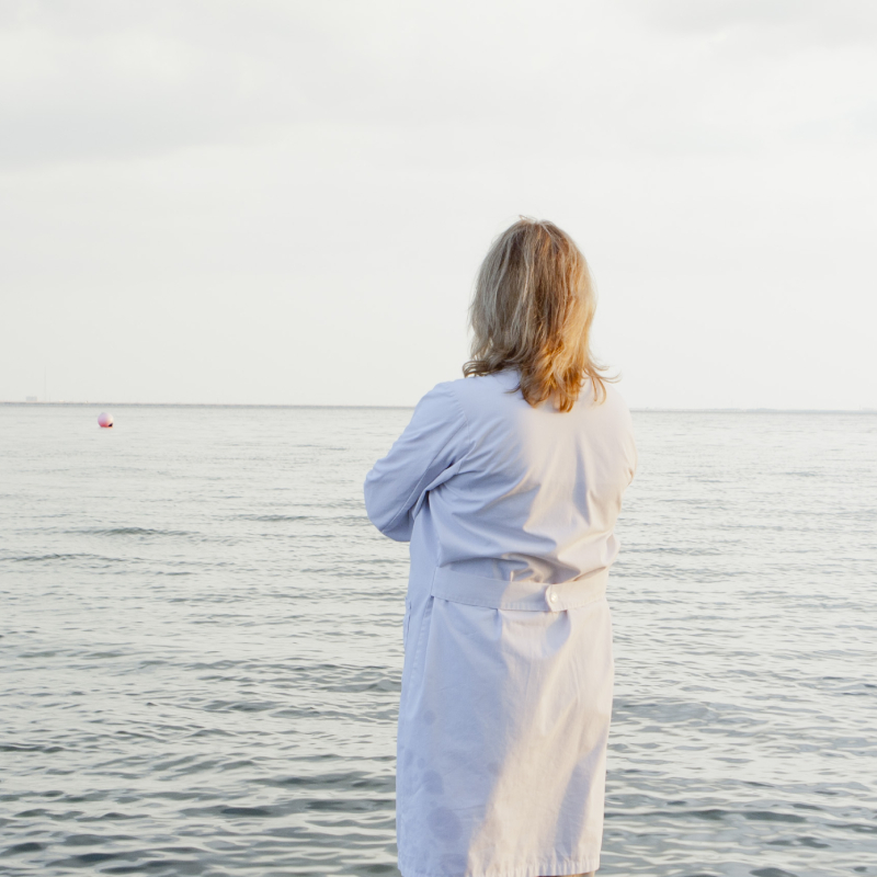 Žena v bílém županu, stojící ve vodě na pláži