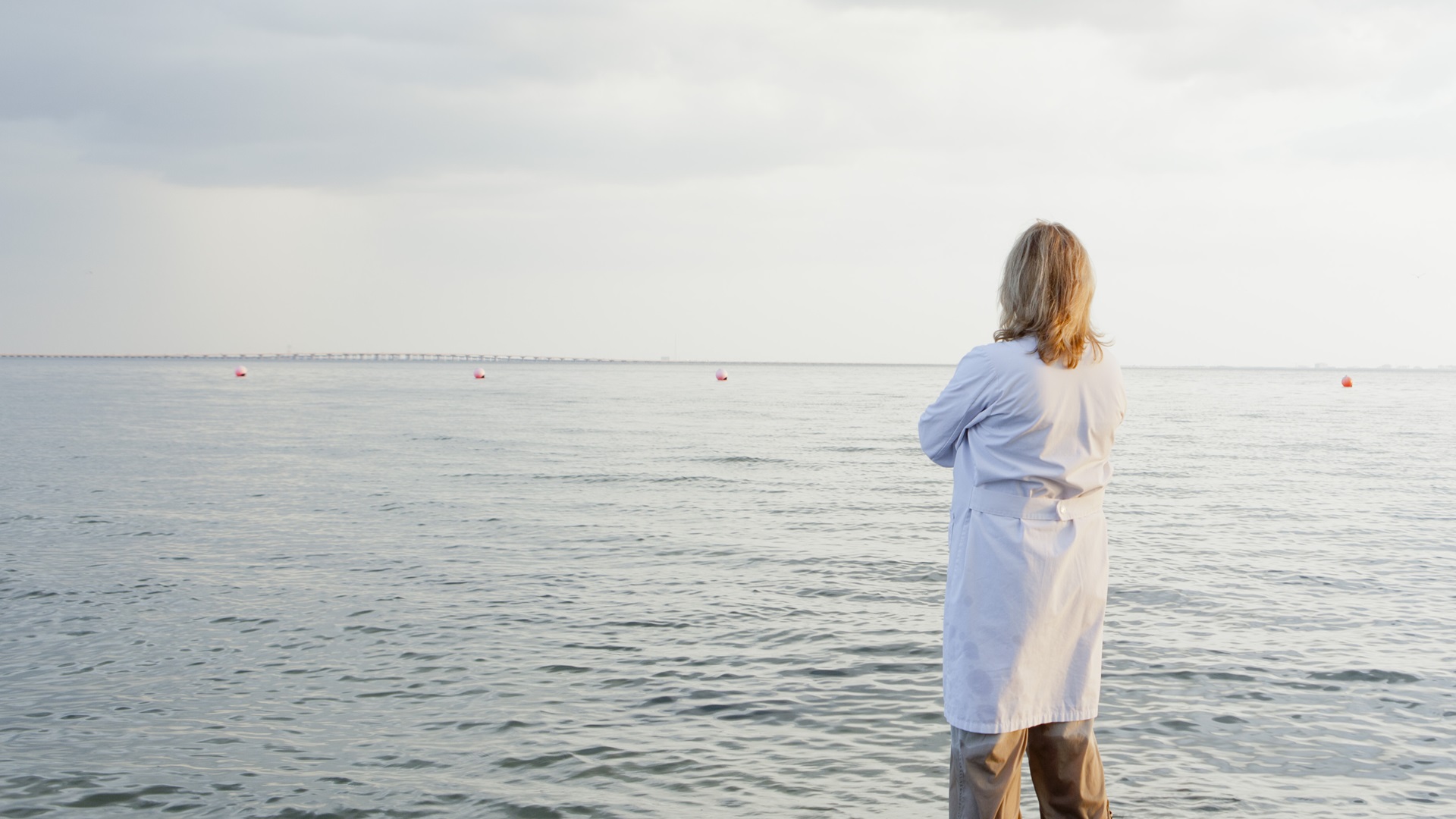 Žena v bílém županu, stojící ve vodě na pláži