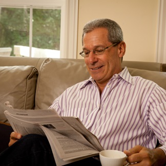 Muž, sedící na pohovce, pijící kávu a čte noviny