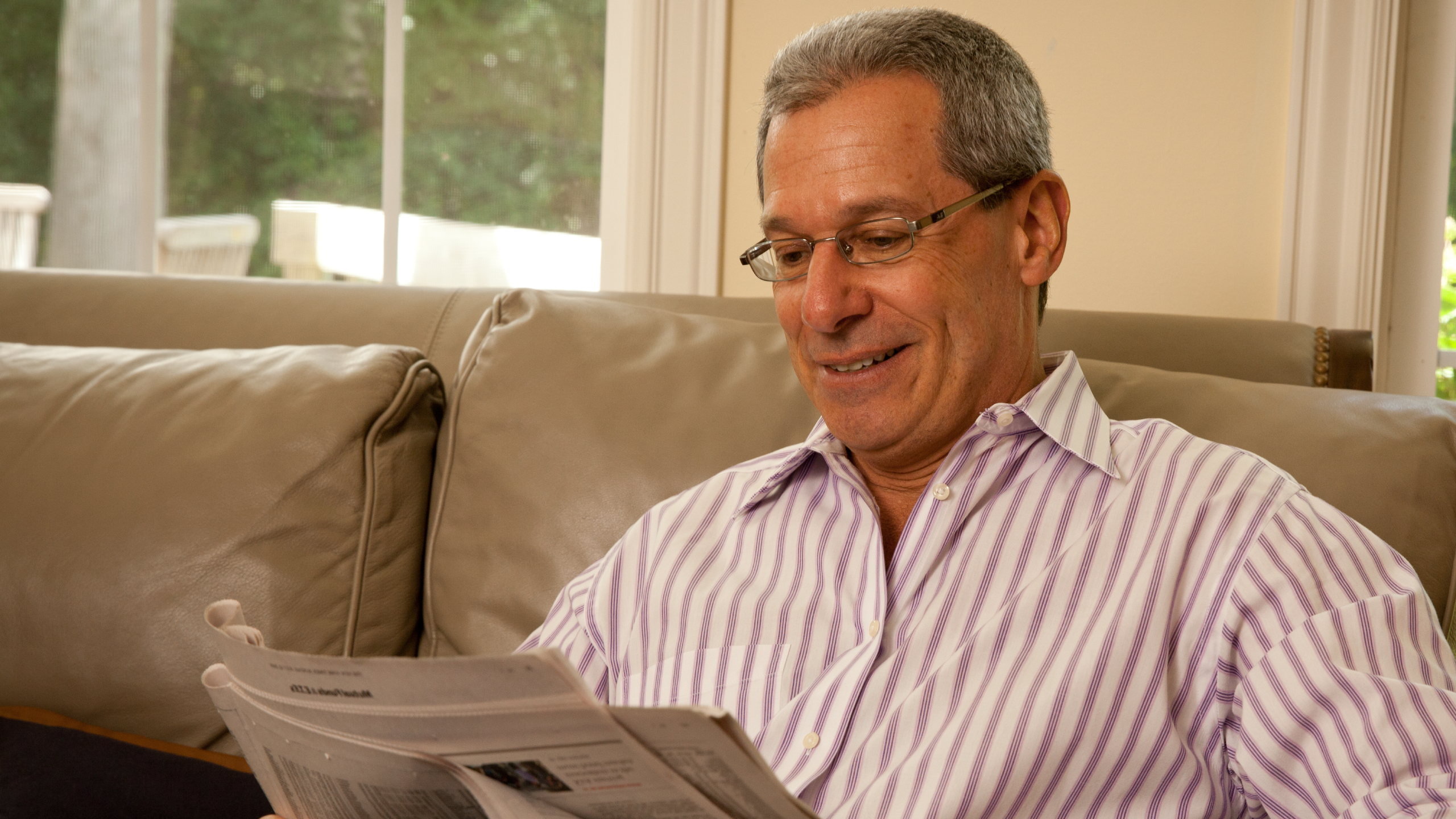Muž, sedící na pohoce, pijící kávu a čte noviny